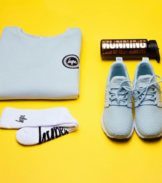 Stylish fashion flat lay with sneakers, sweatshirt, socks, and bottle on yellow background.