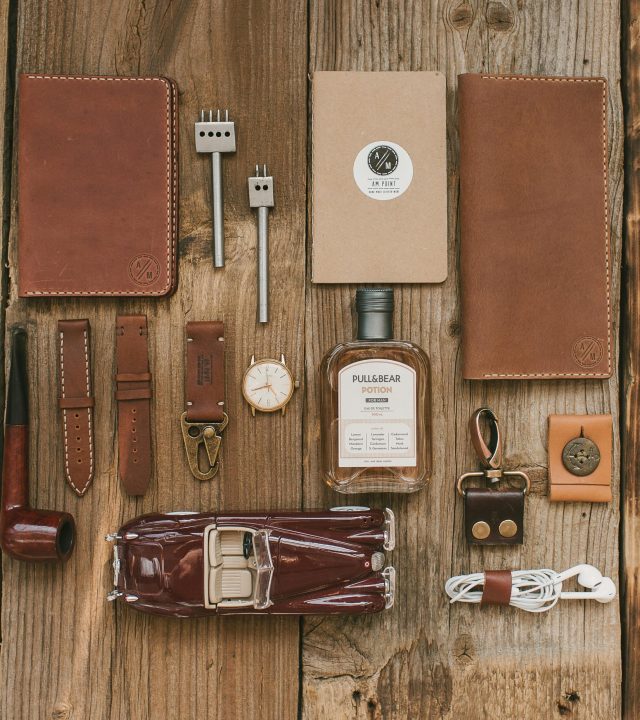 Flat lay showcasing leather accessories, a vintage car model, and modern essentials on a wooden surface.